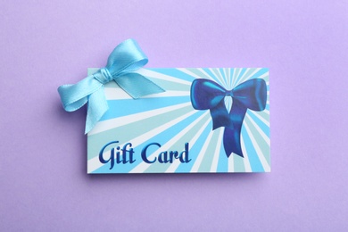 Photo of Gift card with bow on violet background, top view