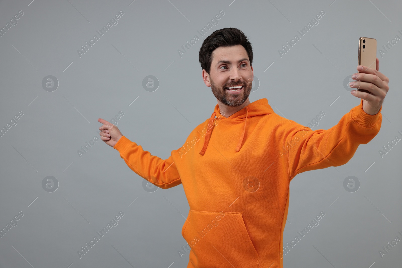 Photo of Smiling man taking selfie with smartphone on grey background, space for text