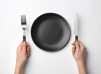 Woman with fork, knife and empty plate on white background, top view