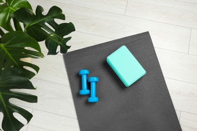 Photo of Exercise mat, yoga block and dumbbells on floor indoors, top view