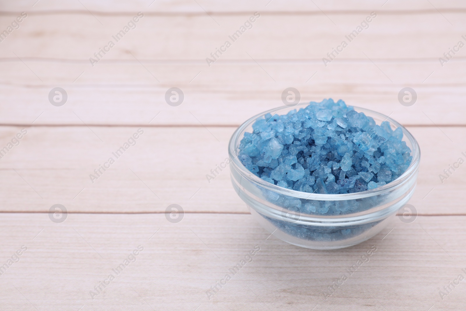 Photo of Bowl with blue sea salt on white wooden table. Space for text