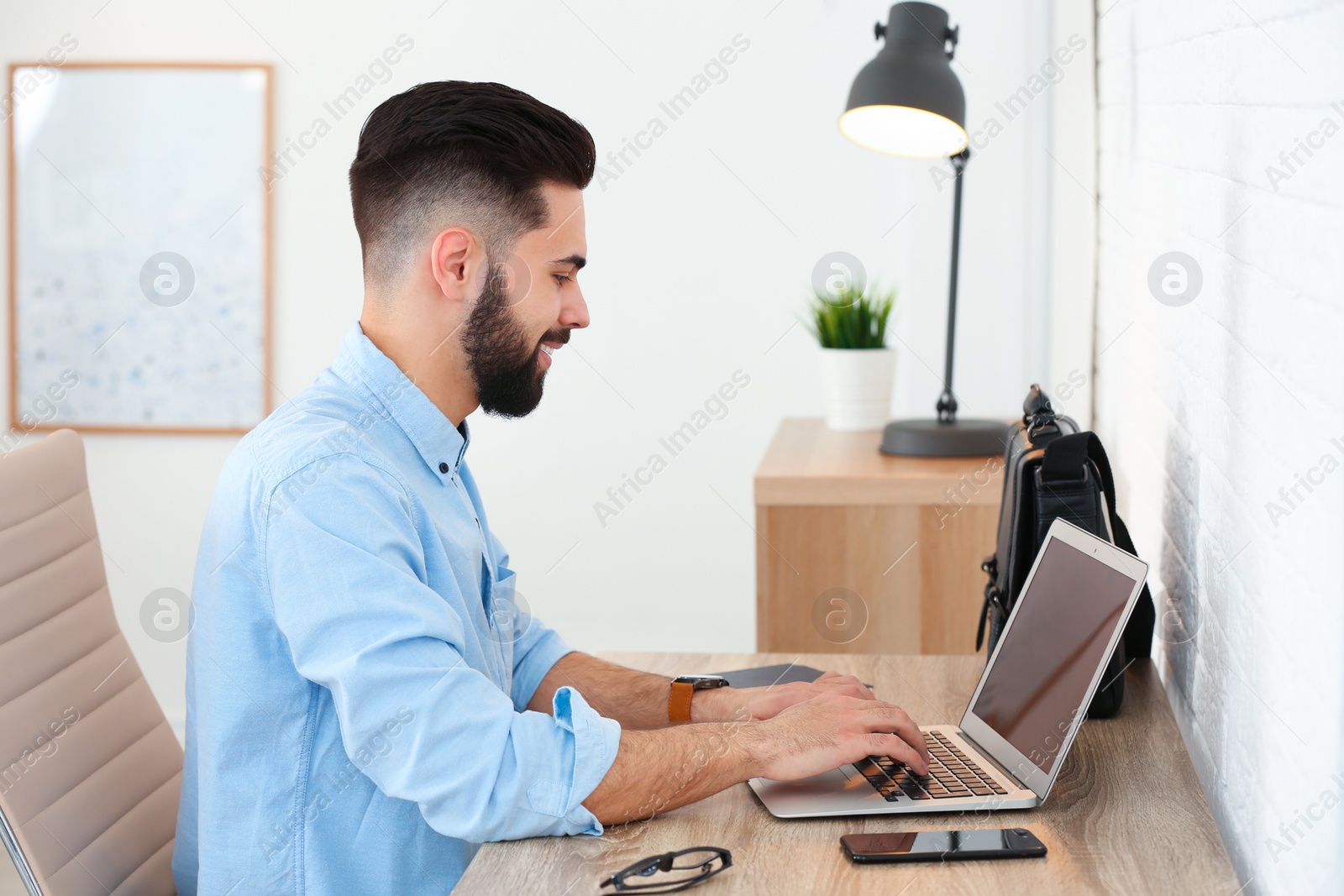 Photo of Handsome young man working with laptop at table in home office