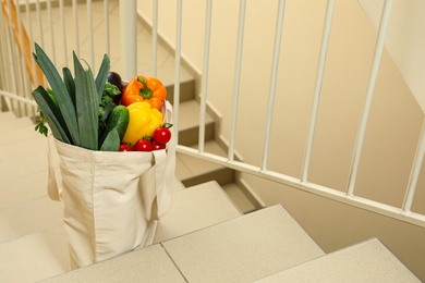 Photo of Tote bag with vegetables on stairs indoors. Space for text