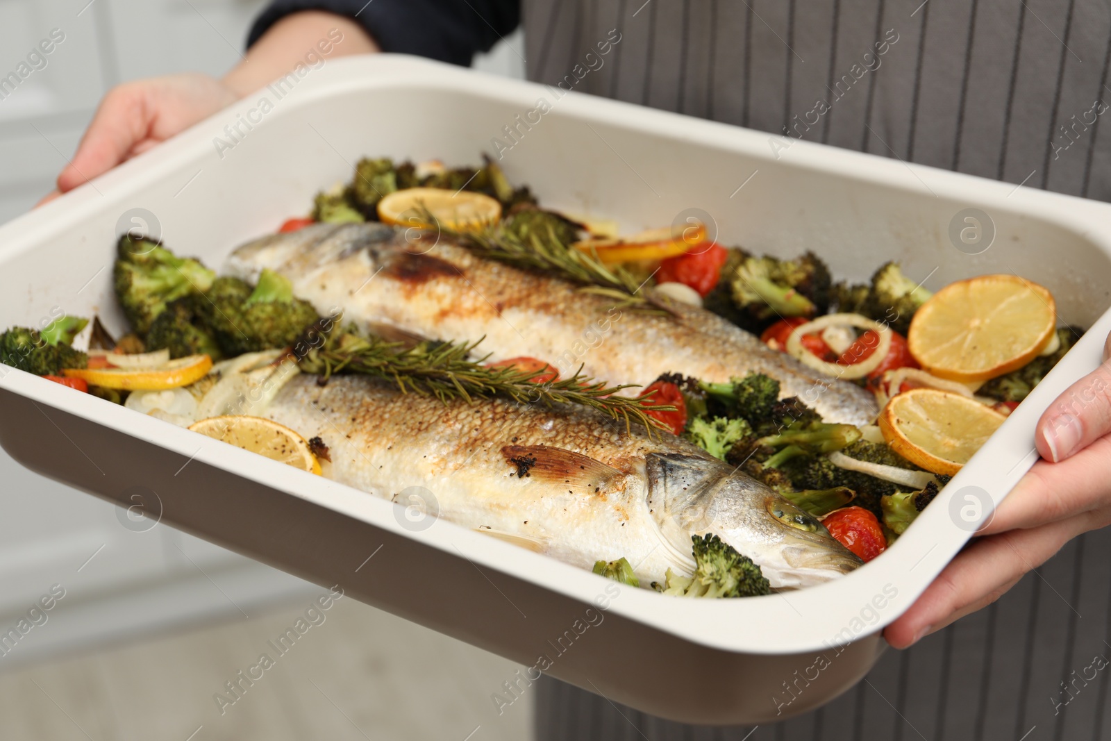 Photo of Woman holding baking dish with delicious fish and vegetables indoors, selective focus