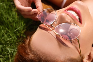 Photo of Beautiful woman in sunglasses on green grass outdoors, closeup