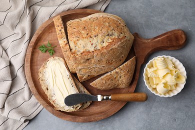 Tasty bread with butter and knife on grey textured table, flat lay
