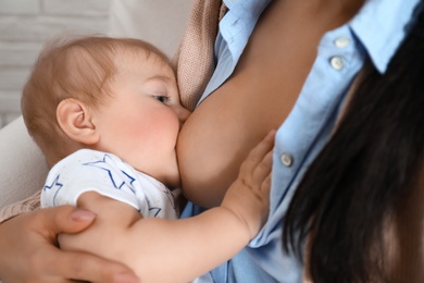 Photo of Woman breast feeding her little baby indoors, closeup