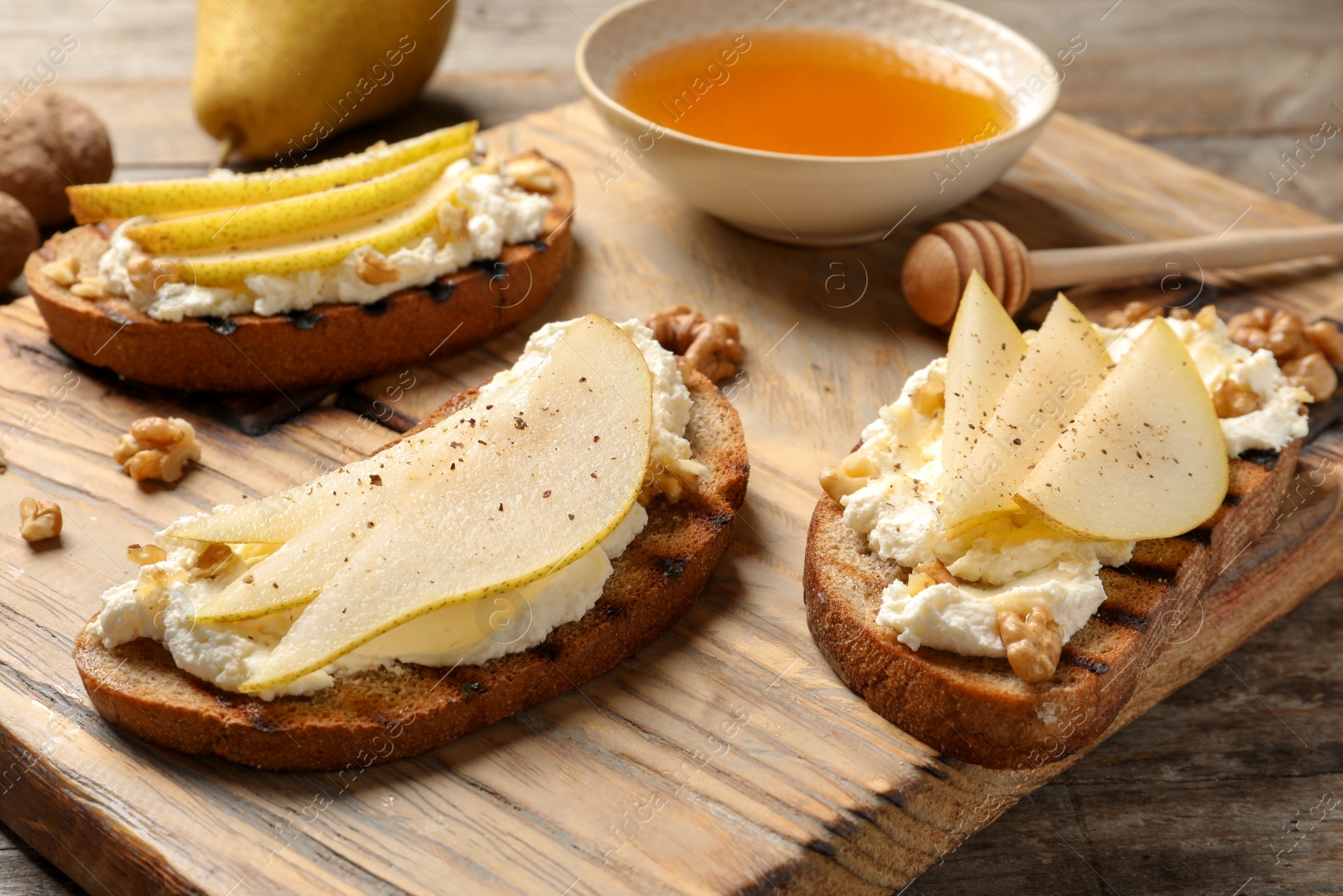 Photo of Toasted bread with tasty cream cheese and pear on wooden board