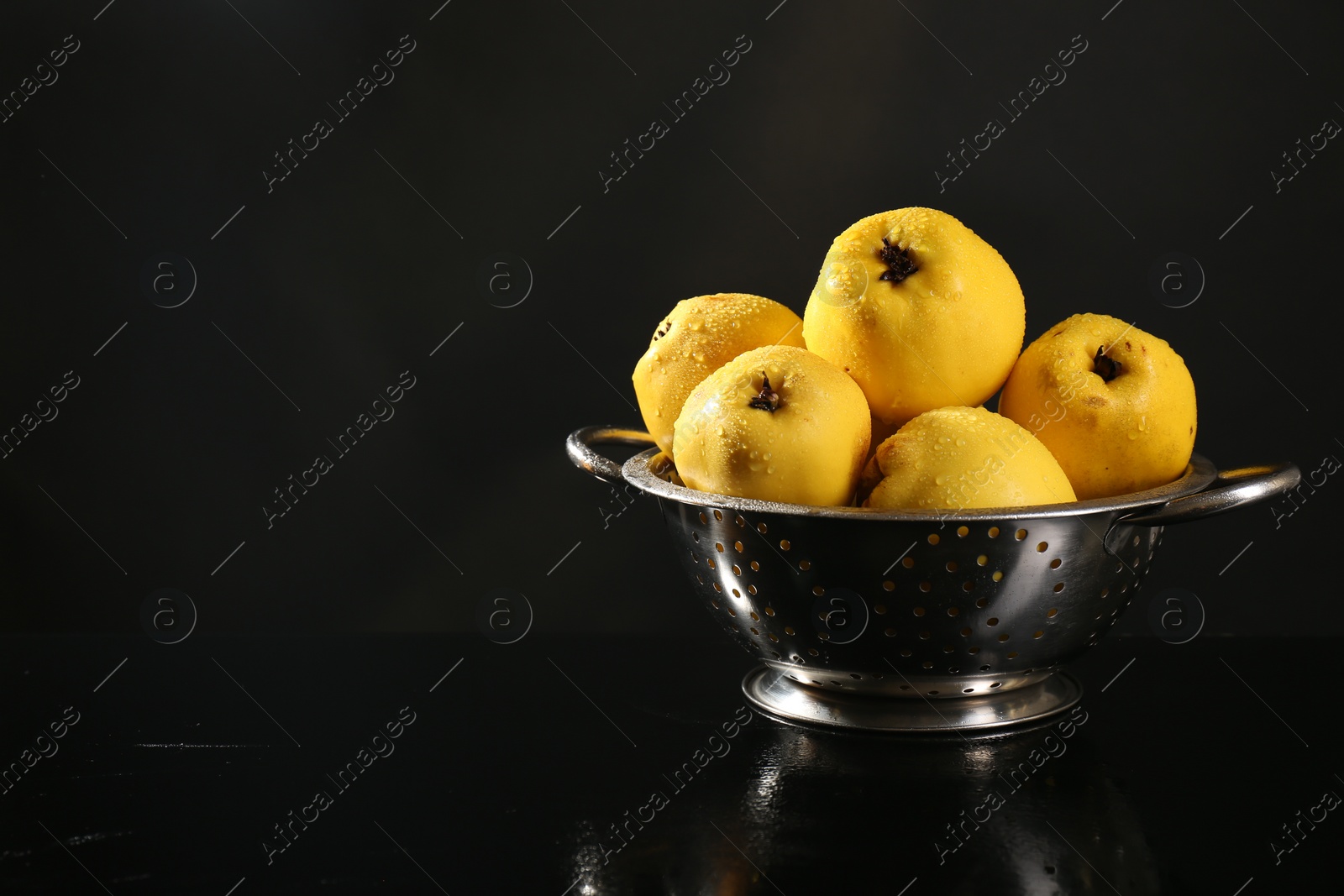 Photo of Tasty ripe quinces with water drops in metal colander on black background, space for text