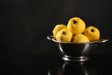 Photo of Tasty ripe quinces with water drops in metal colander on black background, space for text