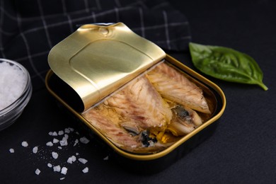 Open tin can with mackerel fillets on black table, closeup