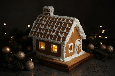 Beautiful gingerbread house decorated with icing and fir branch on grey table