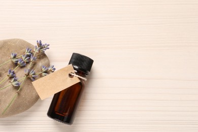 Bottle of essential oil and lavender flowers on white wooden table, flat lay. Space for text