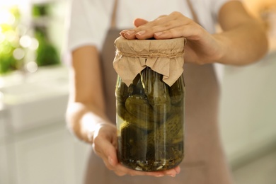 Woman holding jar of pickled cucumbers indoors, closeup