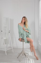 Photo of Pretty young woman in beautiful silk robe sitting on stool at home