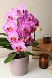 Beautiful blooming orchid, books and burning candle on white table