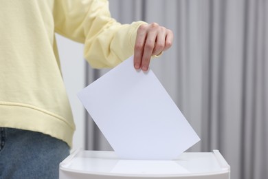 Photo of Woman putting her vote into ballot box on blurred background, closeup