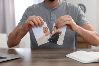 Photo of Man ripping photo at table indoors, closeup. Divorce concept