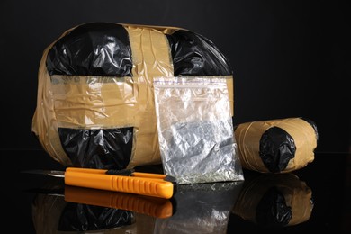 Photo of Smuggling, drug trafficking. Packages with narcotics and utility knife on black mirror surface