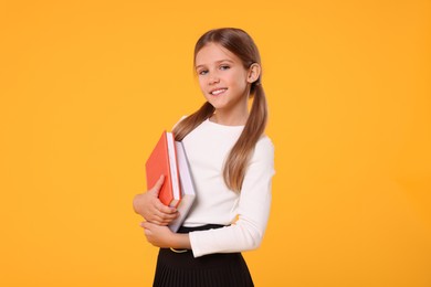 Photo of Happy schoolgirl with books on orange background