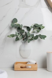 Silicone vase with eucalyptus branches on white marble wall over countertop in stylish bathroom