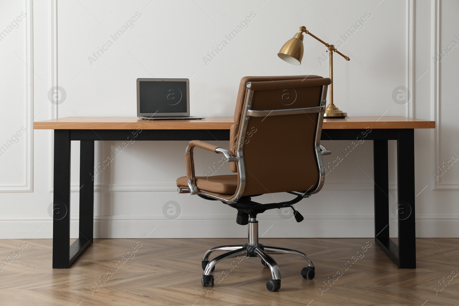 Photo of Stylish workplace with laptop and comfortable armchair near white wall indoors. Interior design