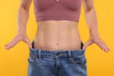 Photo of Slim woman wearing big jeans on yellow background, closeup. Weight loss