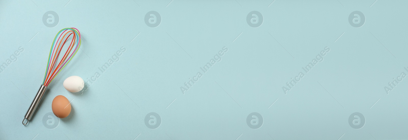 Image of Whisk and eggs on light blue background, flat lay. Banner design with space for text