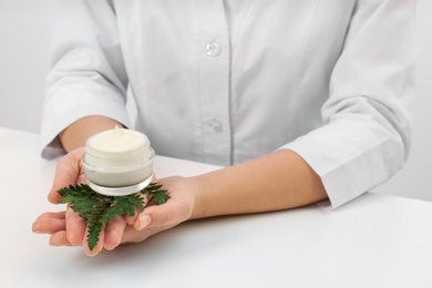 Photo of Female dermatologist holding jar of skin care product at table, closeup