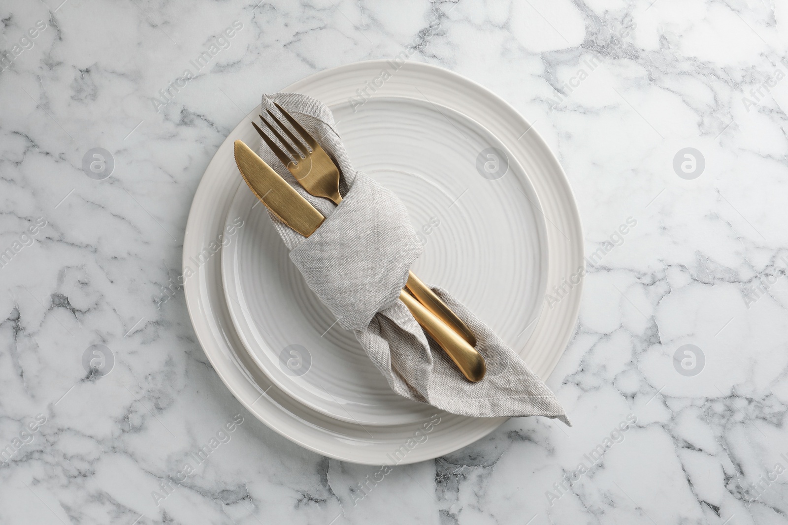 Photo of Stylish setting with cutlery, napkin and plates on white marble table, top view