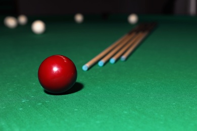 Red billiard ball and cues on table. Space for text