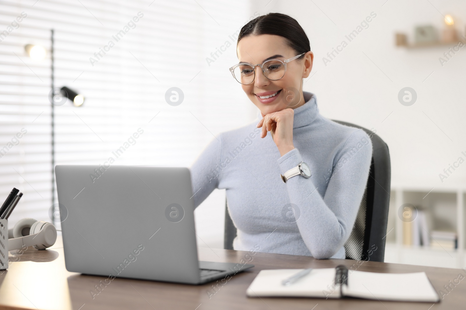 Photo of Young woman in glasses watching webinar at table in office