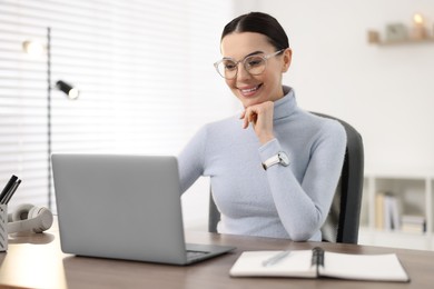 Young woman in glasses watching webinar at table in office