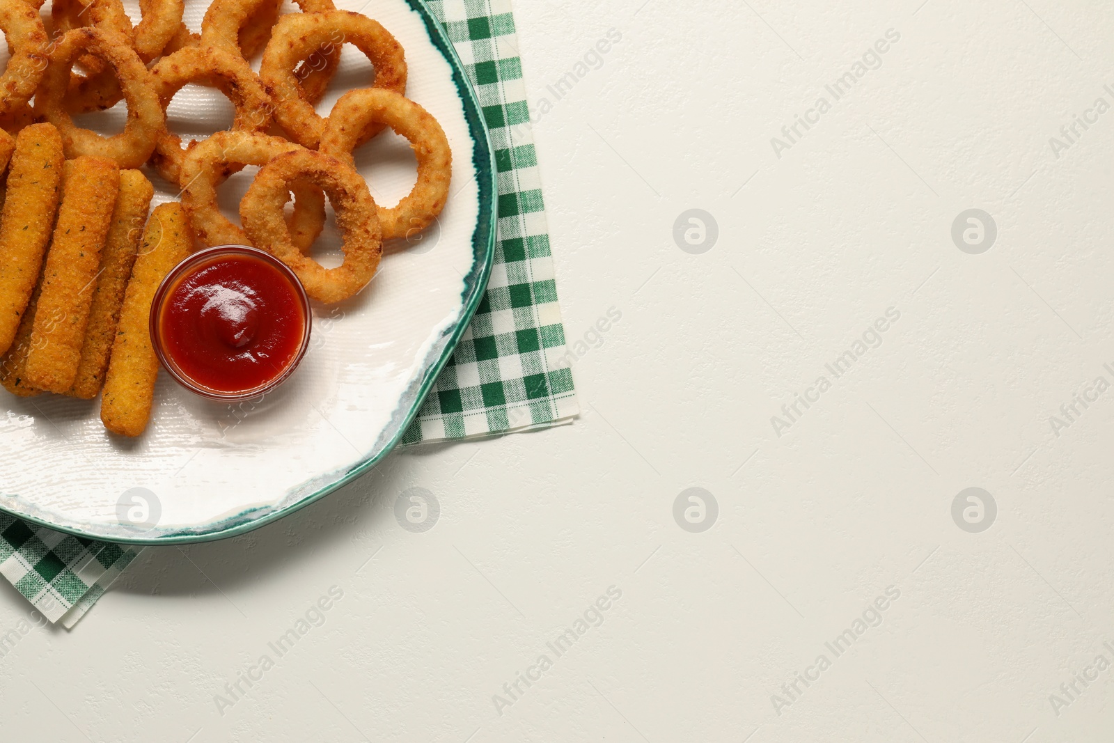 Photo of Plate with tasty ketchup, cheese sticks and onion rings on white table, top view. Space for text