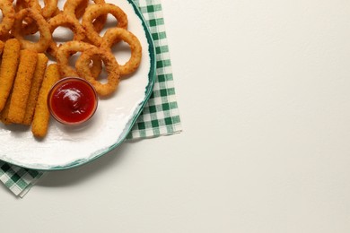 Plate with tasty ketchup, cheese sticks and onion rings on white table, top view. Space for text