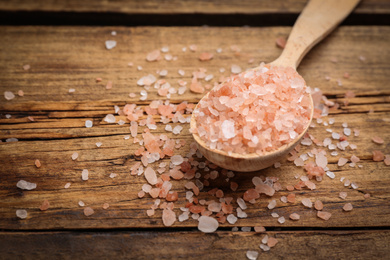 Photo of Spoon and pink himalayan salt on wooden table, closeup