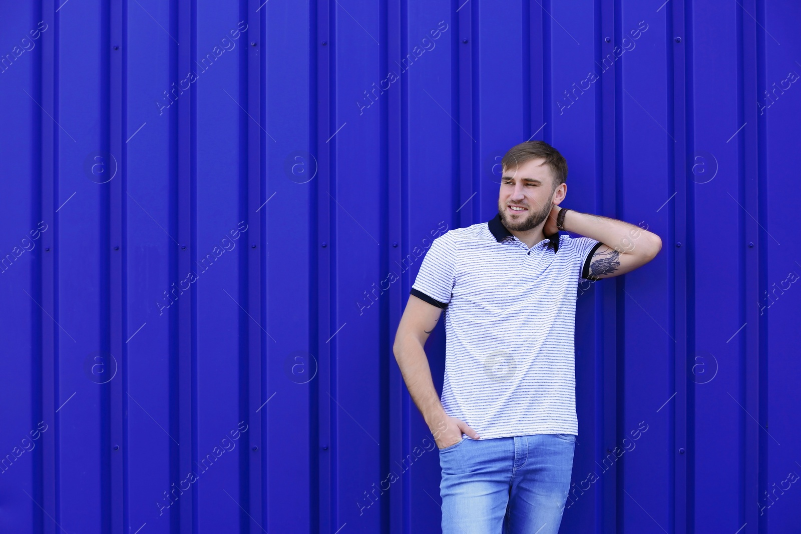 Photo of Young hipster man in stylish jeans posing near color wall