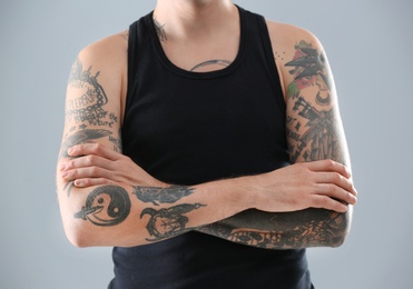 Young man with stylish tattoos on grey background