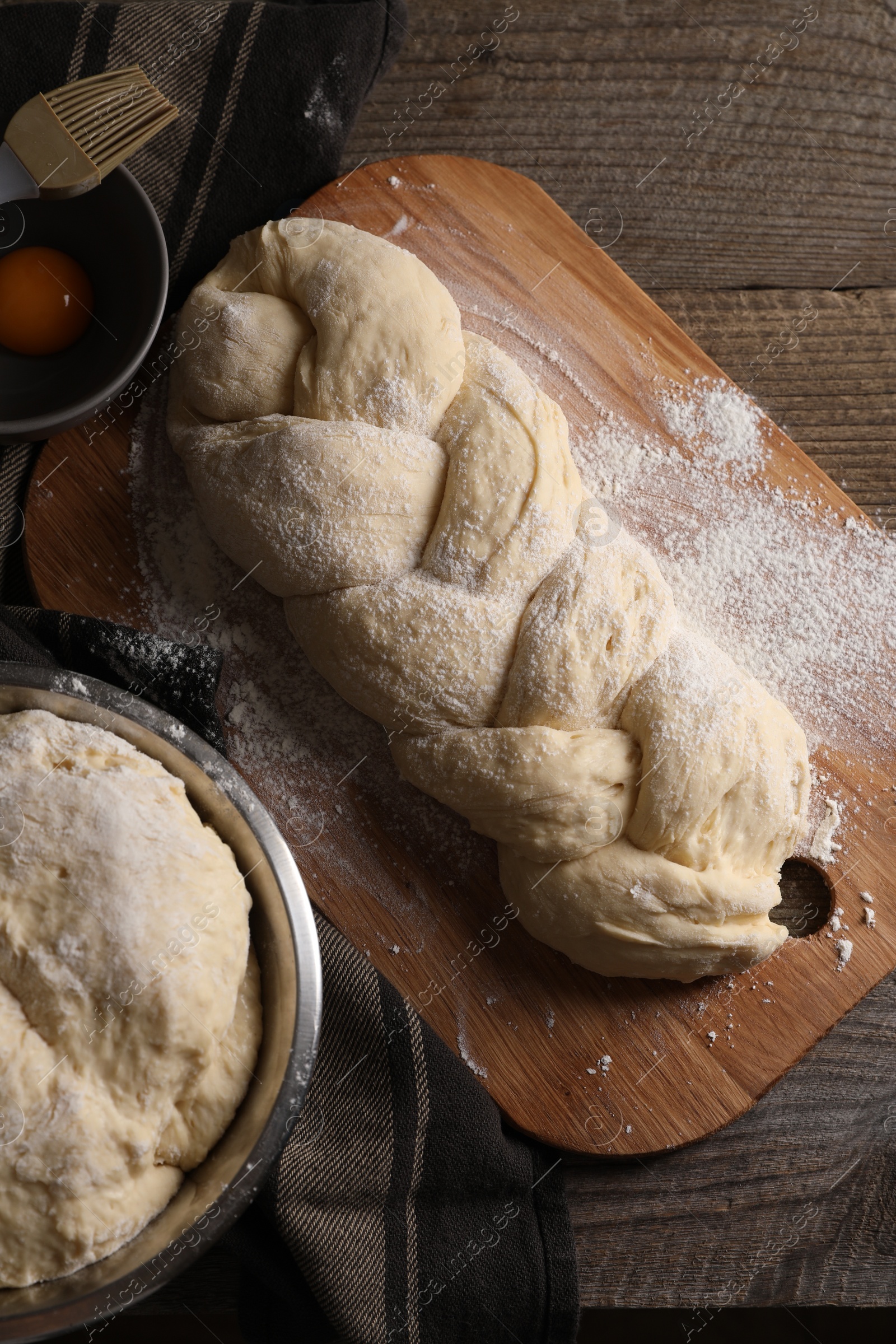 Photo of Homemade braided bread and ingredients on wooden table, flat lay. Cooking traditional Shabbat challah