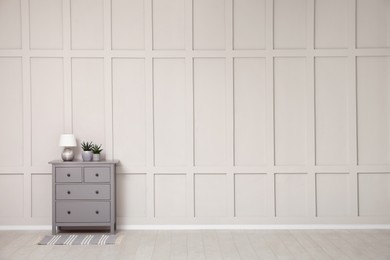 Photo of Grey chest of drawers near empty molding wall indoors, space for text