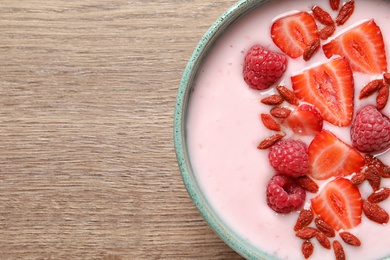 Smoothie bowl with goji berries on wooden table, top view. Space for text