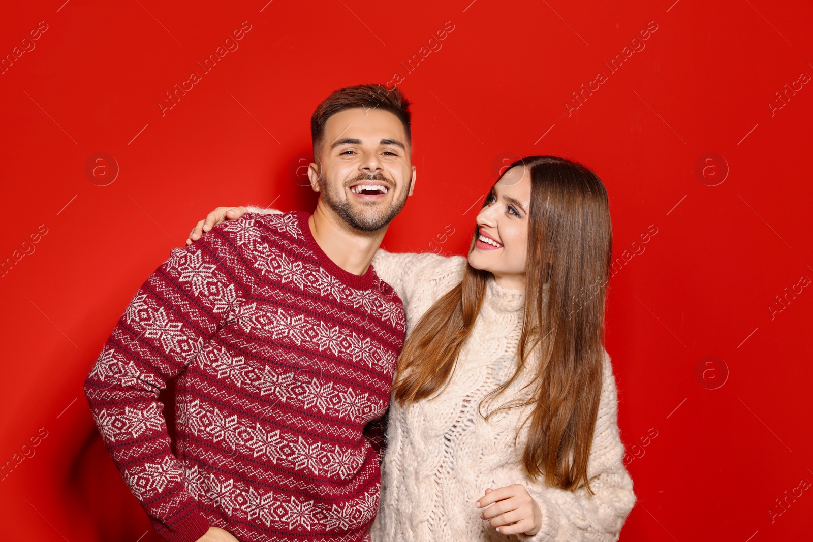 Photo of Couple wearing Christmas sweaters on red background