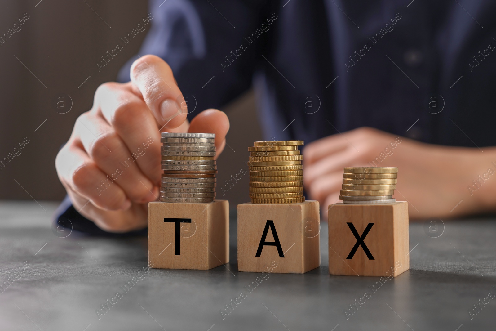 Photo of Woman with word Tax made of wooden cubes and coins at grey table, closeup