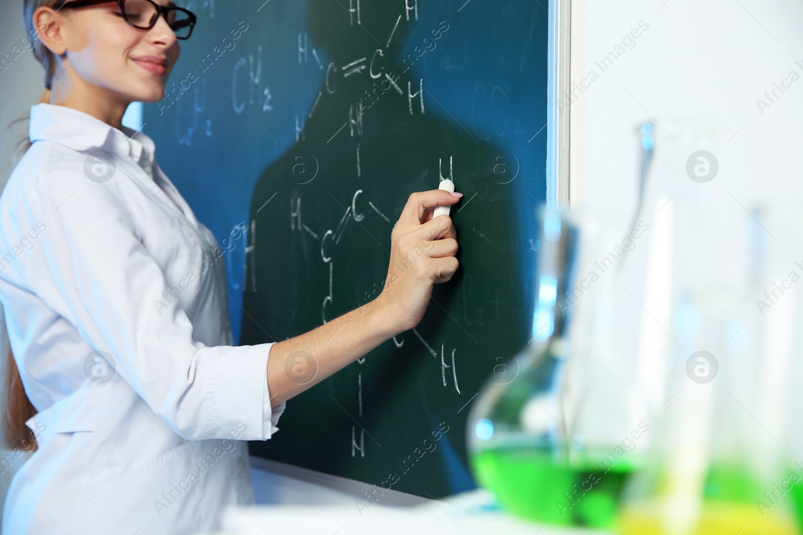 Photo of Female scientist writing chemical formula on chalkboard indoors