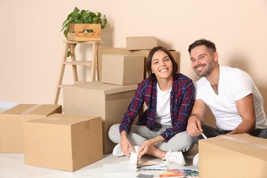 Photo of Happy couple surrounded by moving boxes choosing colors in new apartment