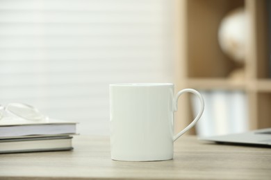 Photo of White ceramic mug and notebooks on wooden table indoors