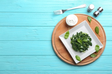 Photo of Tasty cooked spinach served on light blue wooden table, flat lay with space for text. Healthy food