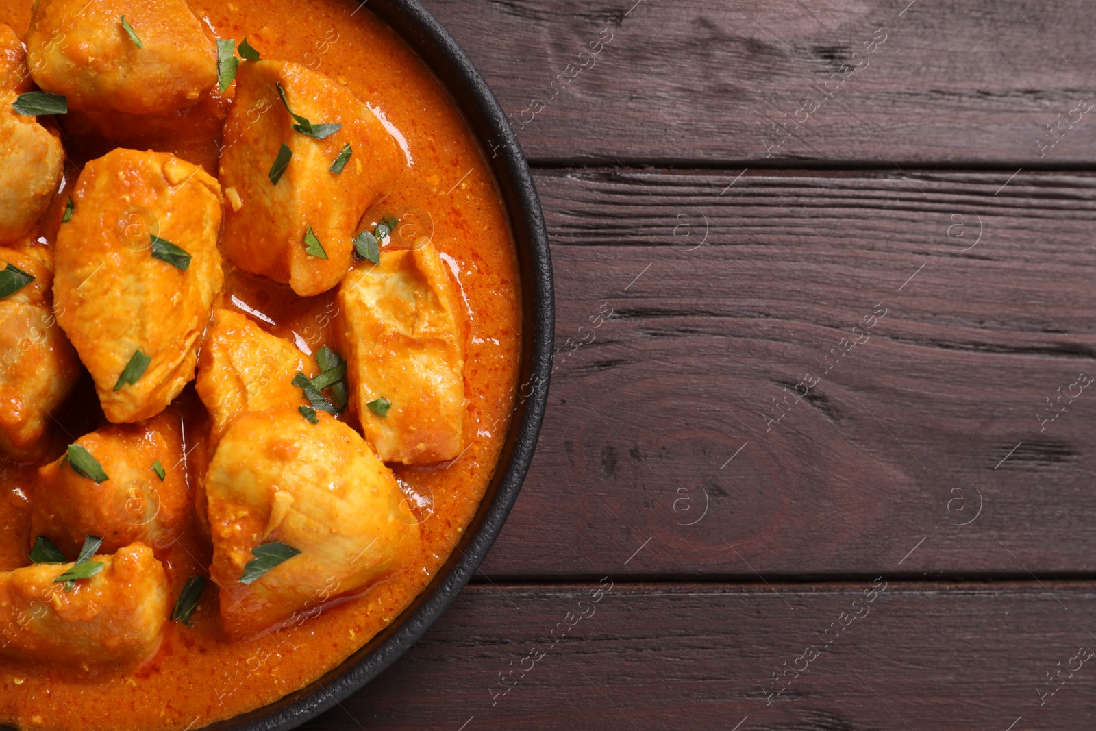 Photo of Delicious chicken curry in pan on wooden table, top view. Space for text