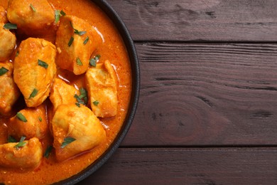 Photo of Delicious chicken curry in pan on wooden table, top view. Space for text