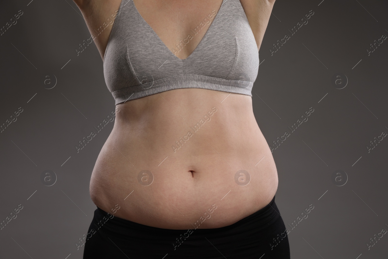 Photo of Woman with excessive belly fat on grey background, closeup. Overweight problem